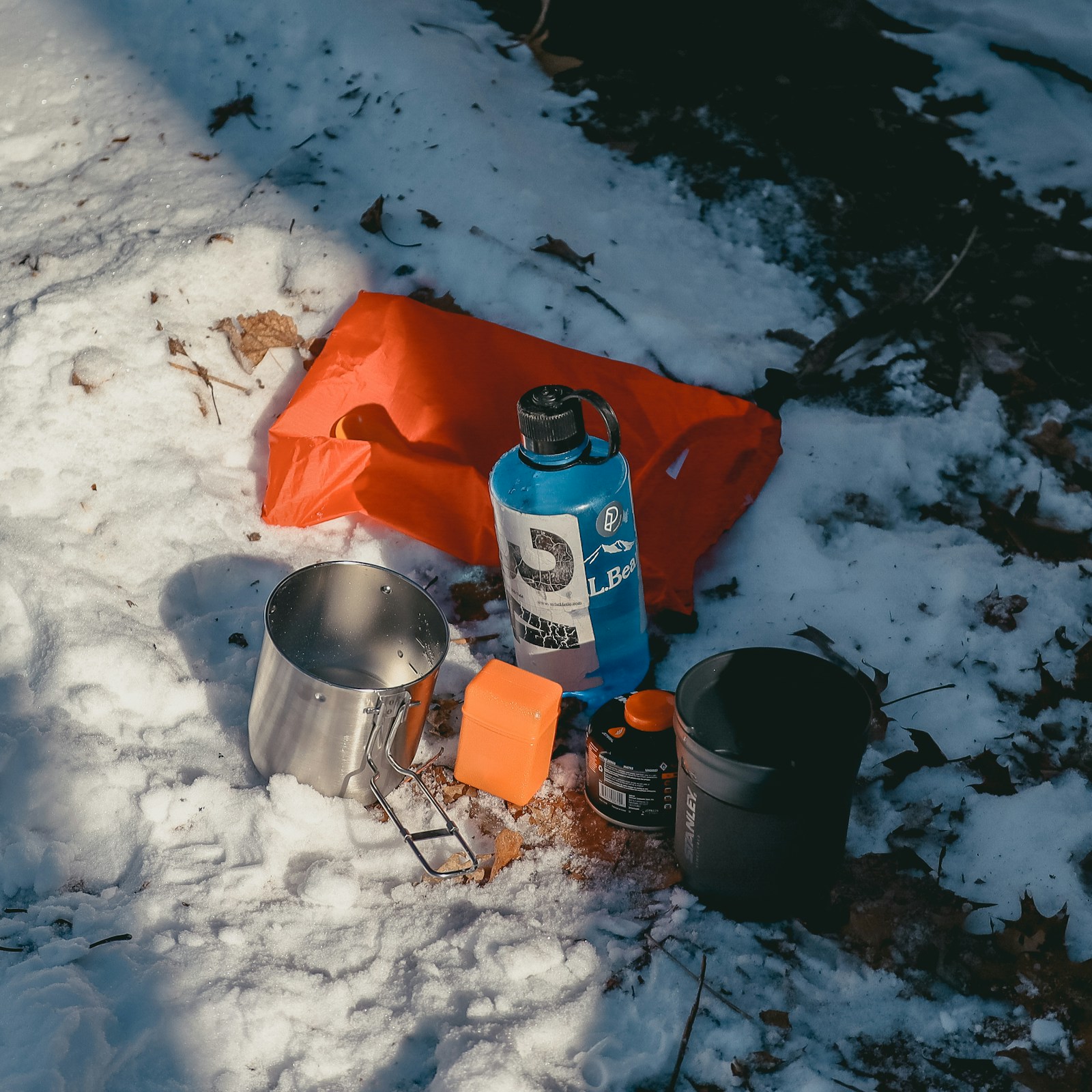 A camp stove and cookset set up on snow at dusk